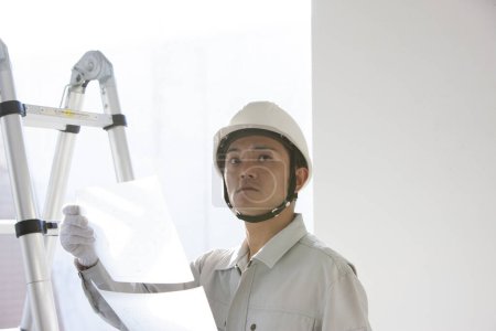 Téléchargez les photos : Portrait du beau jeune constructeur japonais en uniforme sur le chantier - en image libre de droit