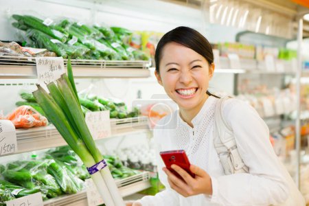 Photo for Smiling Japanese woman with smartphone shopping in grocery store, checking shopping list in phone - Royalty Free Image