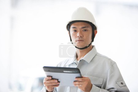 Foto de Retrato de joven constructor japonés guapo en uniforme en el sitio de construcción utilizando tableta digital - Imagen libre de derechos