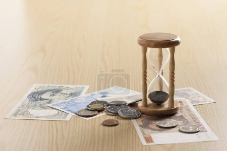 Foto de Reloj de arena y dinero en la mesa de madera. El tiempo es dinero, concepto de negocio - Imagen libre de derechos
