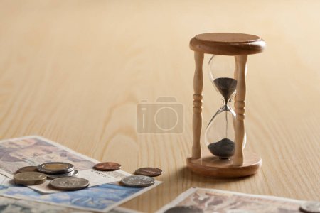Téléchargez les photos : Sablier et argent sur table en bois. Le temps est argent, concept d'entreprise - en image libre de droit