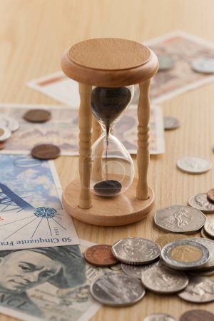 Téléchargez les photos : Sablier et argent sur table en bois. Le temps est argent, concept d'entreprise - en image libre de droit