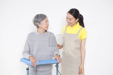 Foto de Amistoso cuidador ayudar discapacitado mayor asiático mujer de pie con walker - Imagen libre de derechos
