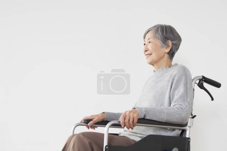 Photo for Smiling elderly asian woman sitting in wheelchair on white background - Royalty Free Image