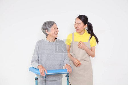 Photo for Female Caregiver helping disabled older asian woman standing with walker - Royalty Free Image