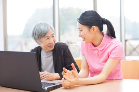 Foto de Joven mujer asiática enseñando anciana a usar laptop en casa - Imagen libre de derechos