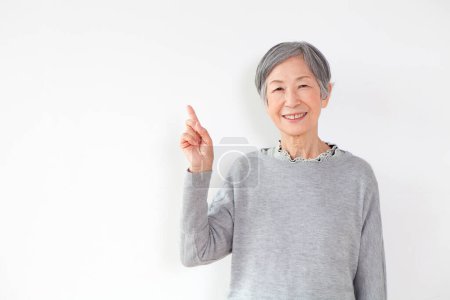 Photo for Senior woman smiling at camera and pointing up with finger on white background - Royalty Free Image