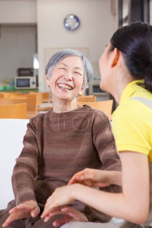Foto de Feliz mujer cuidador ayudar más viejo asiático mujer en sofá - Imagen libre de derechos
