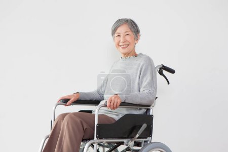 Téléchargez les photos : Sourire vieille asiatique femme assise en fauteuil roulant sur fond blanc - en image libre de droit