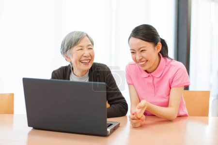 Foto de Joven mujer asiática enseñando anciana a usar laptop en casa - Imagen libre de derechos