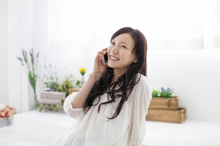 Foto de Retrato de hermosa joven mujer asiática usando teléfono inteligente en el interior de la casa luz - Imagen libre de derechos