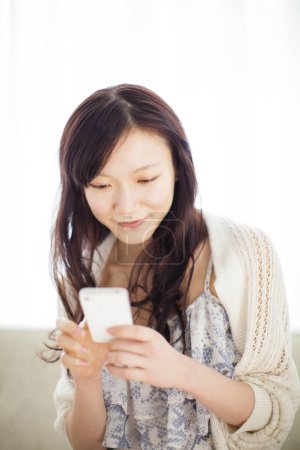 Téléchargez les photos : Portrait de belle jeune femme asiatique en utilisant smartphone à l'intérieur de la maison lumière - en image libre de droit