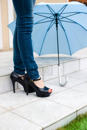 Photo for Female legs in high heels and blue umbrella - Royalty Free Image