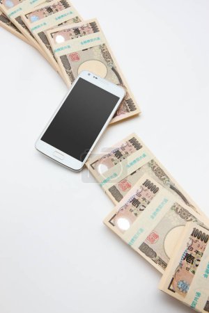 Téléchargez les photos : Smartphone avec argent yen japonais sur fond blanc. vue de dessus. - en image libre de droit