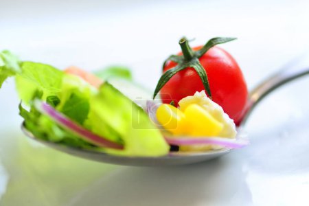 Foto de Ensalada con verduras frescas en cuchara, primer plano. Tomate cereza, huevo, rodajas de zanahoria y pepino, hojas de lechuga - Imagen libre de derechos