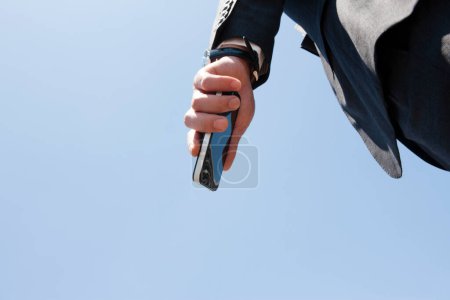 Téléchargez les photos : Main d'homme d'affaires tenant un smartphone sur ciel bleu - en image libre de droit
