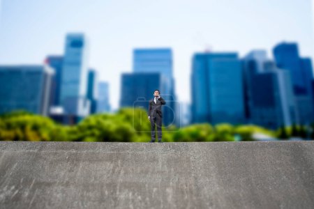 Téléchargez les photos : Homme d'affaires debout sur le dessus du bâtiment en béton contre le paysage urbain flou - en image libre de droit