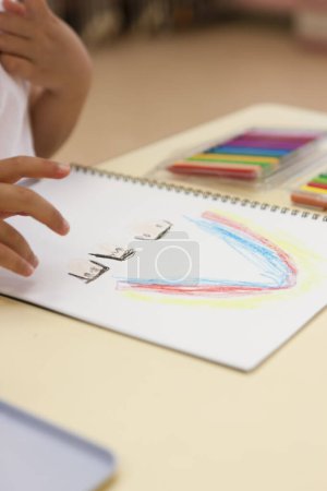 Photo for Little girl drawing rainbow with color pencils in classroom - Royalty Free Image