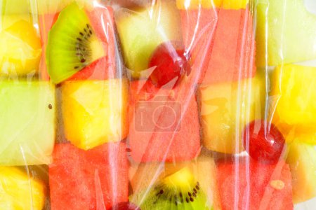 Téléchargez les photos : Gros plan de salade de fruits frais avec pastèque, ananas, raisins et kiwis recouverts d'une feuille transparente - en image libre de droit
