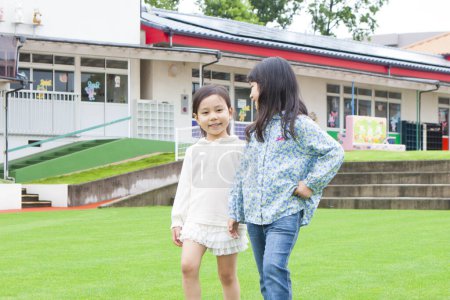 Foto de Lindo asiático niñas caminando juntos en el patio de la escuela. Feliz poco amigos divirtiéndose - Imagen libre de derechos