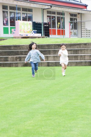 Téléchargez les photos : Portrait de deux petites filles asiatiques souriantes courant sur l'herbe verte - en image libre de droit
