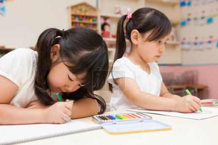 Photo for Two concentrated asian little schoolgirls drawing in classroom - Royalty Free Image
