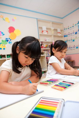 Photo for Two little asian schoolgirls drawing in classroom - Royalty Free Image
