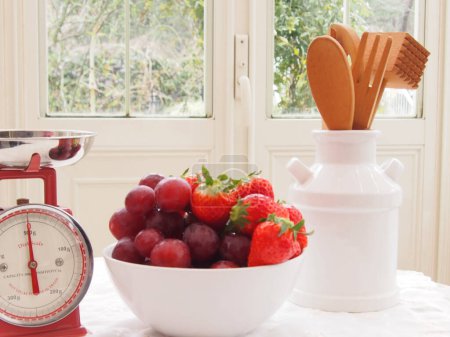 Téléchargez les photos : Fraises fraîches mûres et raisins dans un bol avec des balances de cuisine rétro sur la table - en image libre de droit