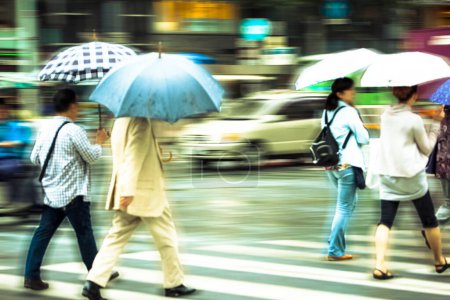 Téléchargez les photos : Vue floue des personnes avec des parasols marchant dans la rue de la ville sous la pluie - en image libre de droit