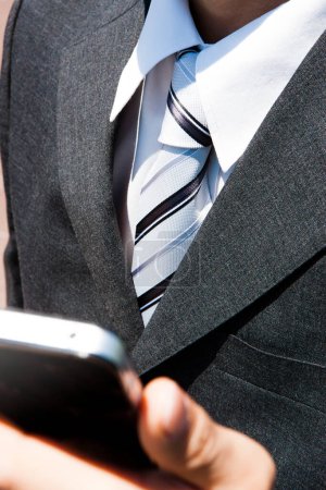 Téléchargez les photos : Homme d'affaires en costume formel tenant smartphone sur ciel bleu - en image libre de droit