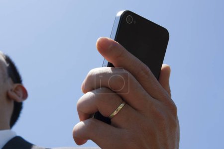 Téléchargez les photos : Homme d'affaires en costume formel tenant smartphone sur ciel bleu - en image libre de droit
