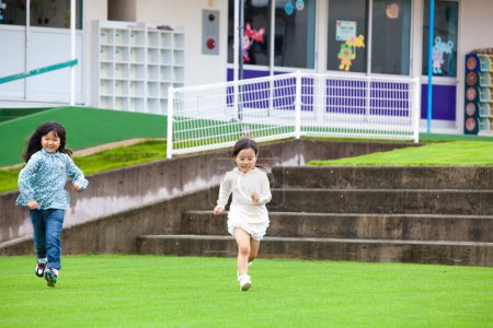 Photo for Portrait of two smiling Asian little girls running on green grass - Royalty Free Image
