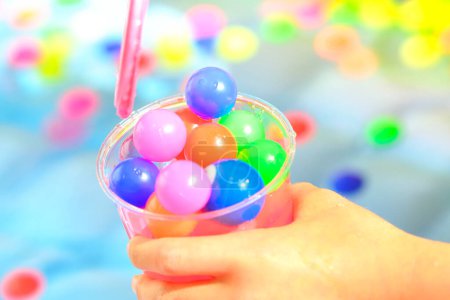 Foto de Taza de plástico de la mano de los niños con bolas pequeñas coloridas - Imagen libre de derechos
