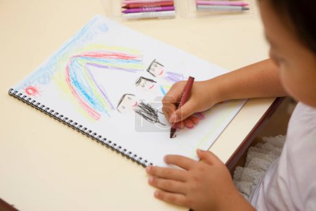Photo for Little girl drawing rainbow and family with color pencils in classroom - Royalty Free Image