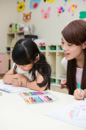 Téléchargez les photos : Portrait de heureux asiatique jeune enseignant et deux petites filles dessin dans la salle de classe - en image libre de droit