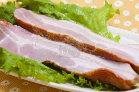 Téléchargez les photos : Tranches de bacon avec des feuilles de salade sur le fond, gros plan - en image libre de droit
