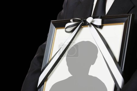 Close-up view of person holding funeral frame with man silhouette 