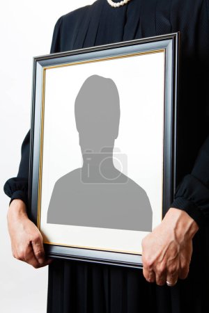 Close-up view of person holding funeral frame with man silhouette 