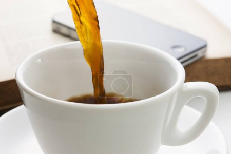 Foto de Cup of coffee, book and phone on white table background, close-up view - Imagen libre de derechos