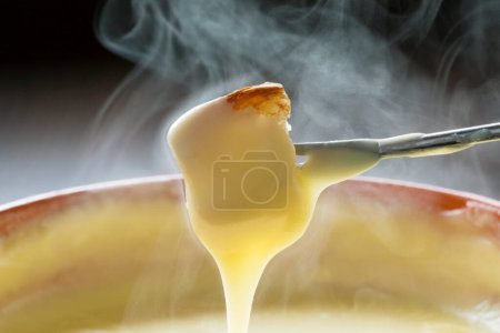 Photo for Melted cheese drips in strings from a chunk of fresh bread in cheese fondue dinner. - Royalty Free Image