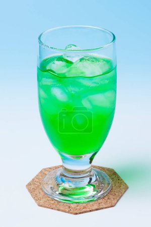 Téléchargez les photos : Verre avec boisson verte et glaçons sur fond bleu clair - en image libre de droit