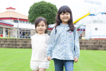 Téléchargez les photos : Portrait de deux écolières asiatiques marchant à l'extérieur tenant la main - en image libre de droit