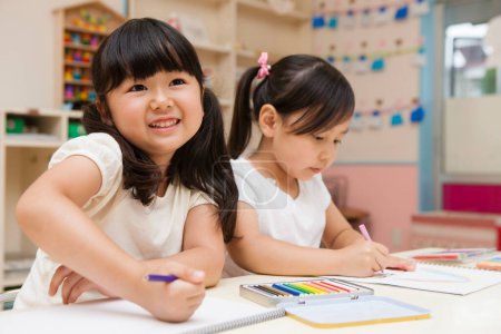 Téléchargez les photos : Deux heureux asiatique petites écolières dessin dans salle de classe - en image libre de droit