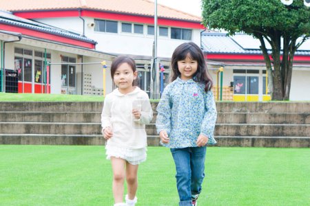 Téléchargez les photos : Deux mignon asiatique écoliers marche sur vert herbe à école cour - en image libre de droit