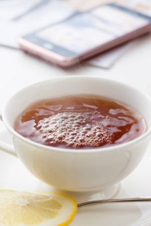 Téléchargez les photos : Une tasse de thé avec une tranche de citron dedans et smartphone - en image libre de droit