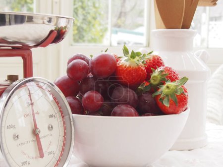 Téléchargez les photos : Fraises fraîches mûres et raisins dans un bol avec des balances de cuisine rétro sur la table - en image libre de droit