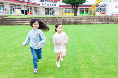 Photo for Portrait of two smiling Asian little girls running on green grass - Royalty Free Image