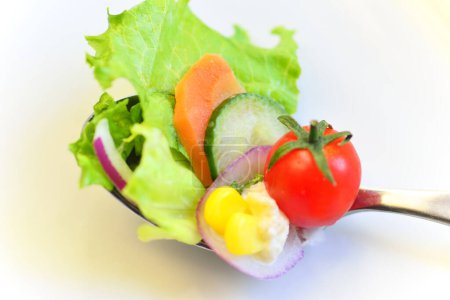 Téléchargez les photos : Salade avec des légumes frais dans la cuillère, gros plan. Tomate cerise, oeuf, tranches de carotte et concombre, feuilles de laitue - en image libre de droit