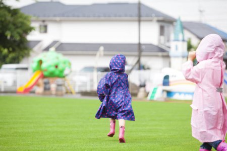 two cute Asian little girls wearing raincoats running in the playground