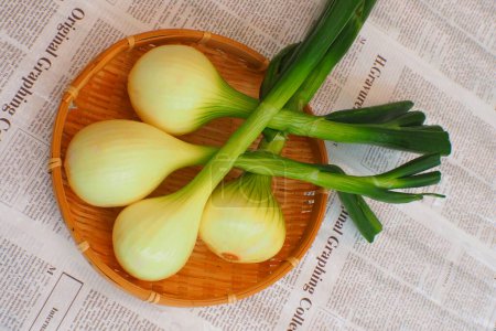 Foto de Primer plano de bulbos de cebolla orgánica fresca en tazón de bambú en el fondo del periódico - Imagen libre de derechos